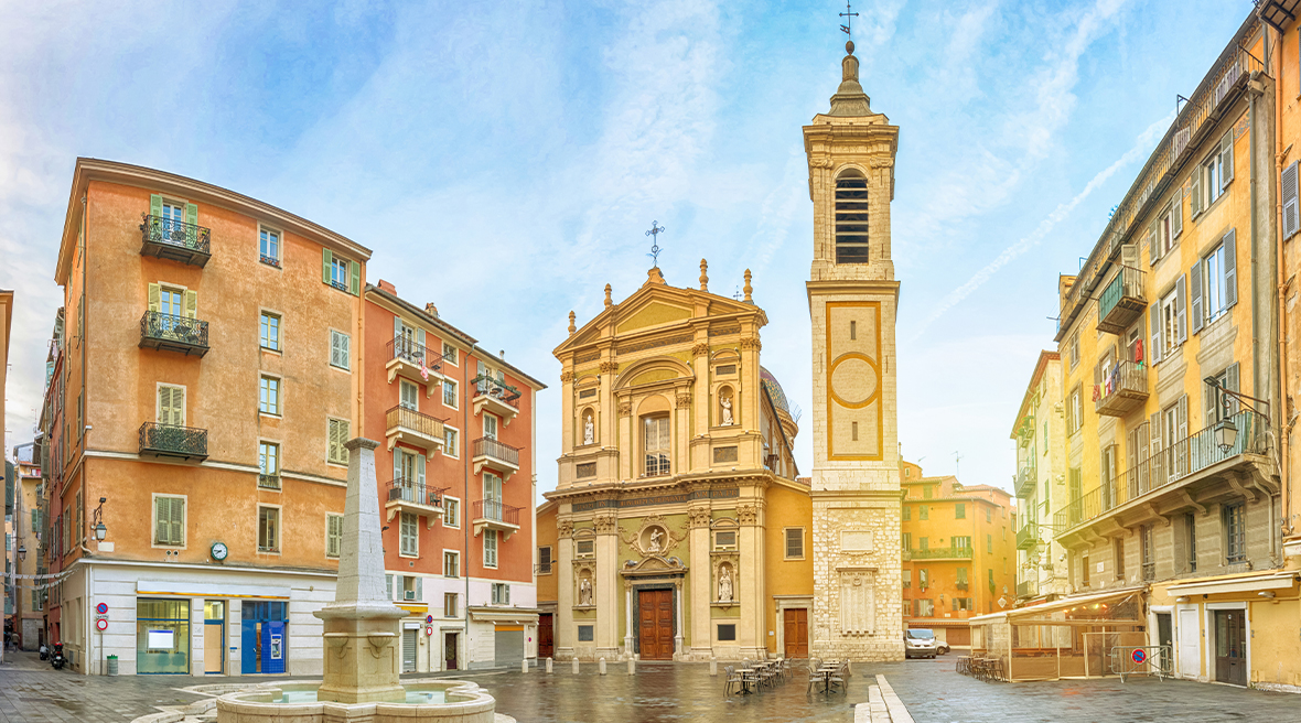 An attractive historic small city square with an Italian style church and bell tower, fountain and pedestrianized area.